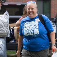 Volunteer smiling at camera with people moving items behind her